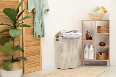 Photo of Wicker basket full of laundry, bathrobe and houseplant in bathroom