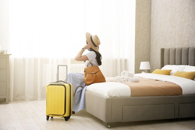 Photo of Traveller with suitcase sitting on bed in hotel room