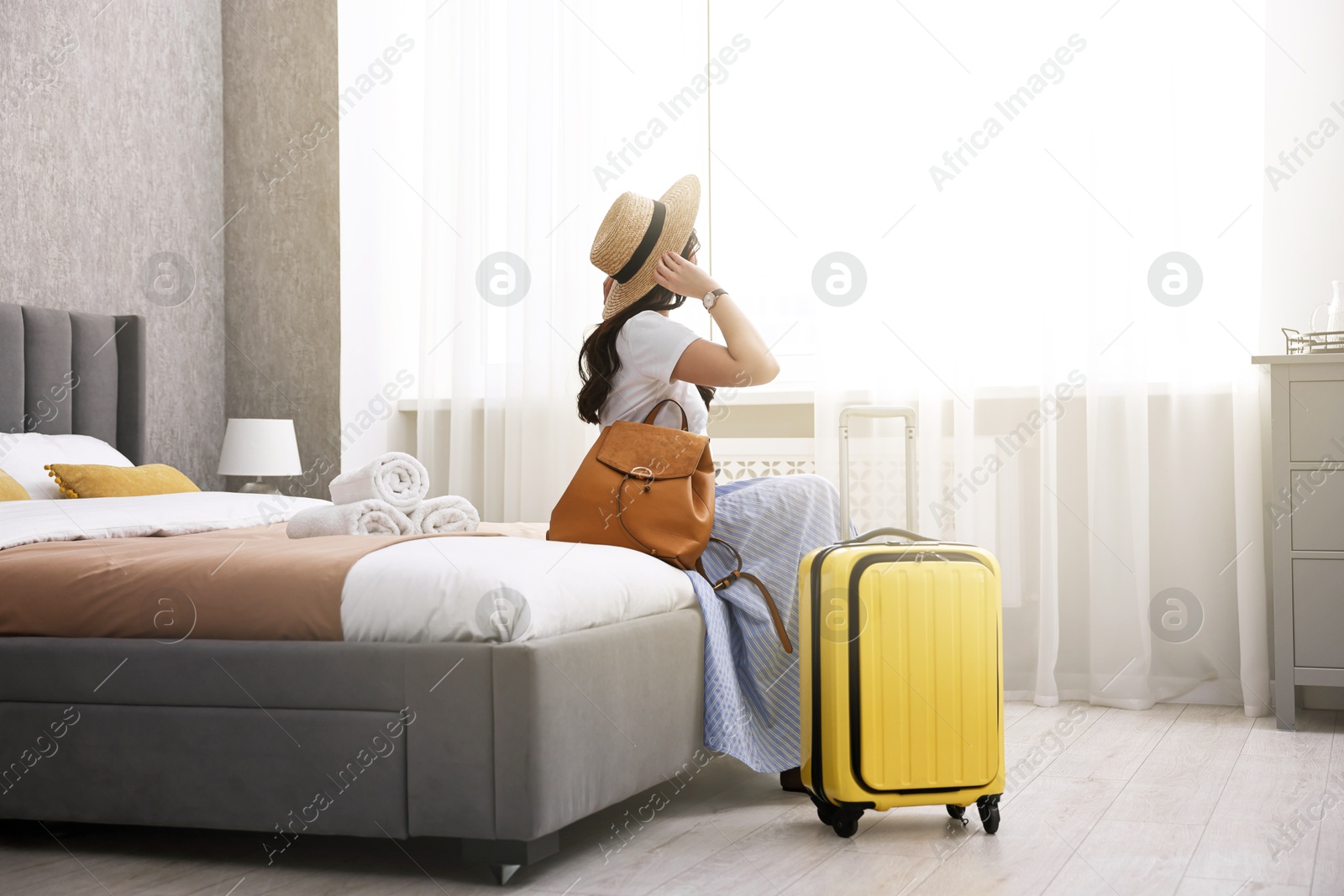 Photo of Traveller with suitcase sitting on bed in hotel room