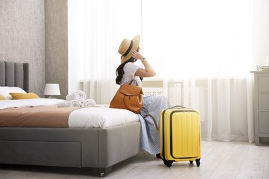 Photo of Traveller with suitcase sitting on bed in hotel room