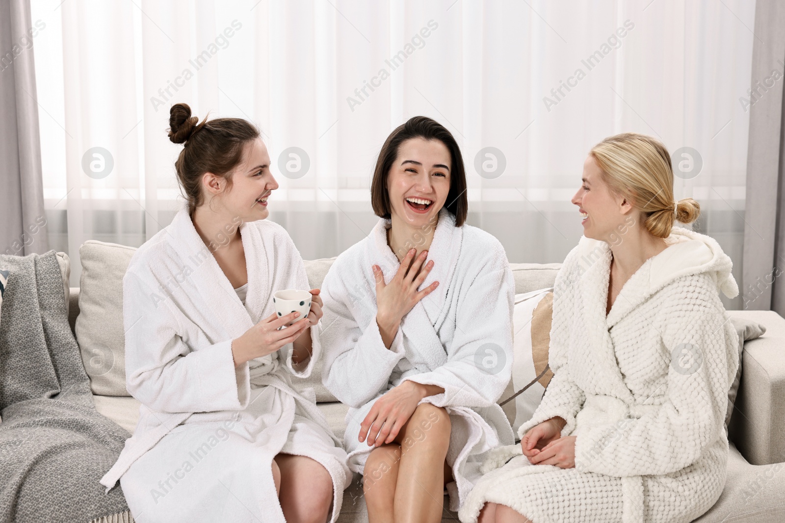 Photo of Cheerful women in bathrobes resting on sofa at spa