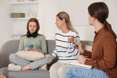 Photo of Teenage girl using smartphone while having consultation with her mom and psychologist indoors