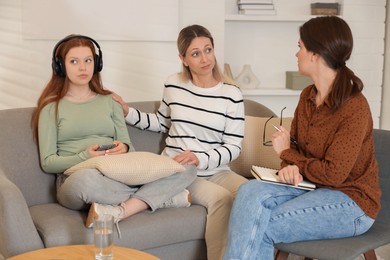 Photo of Teenage girl listening to music instead of working with psychologist in office. Mother and daughter difficult relationship