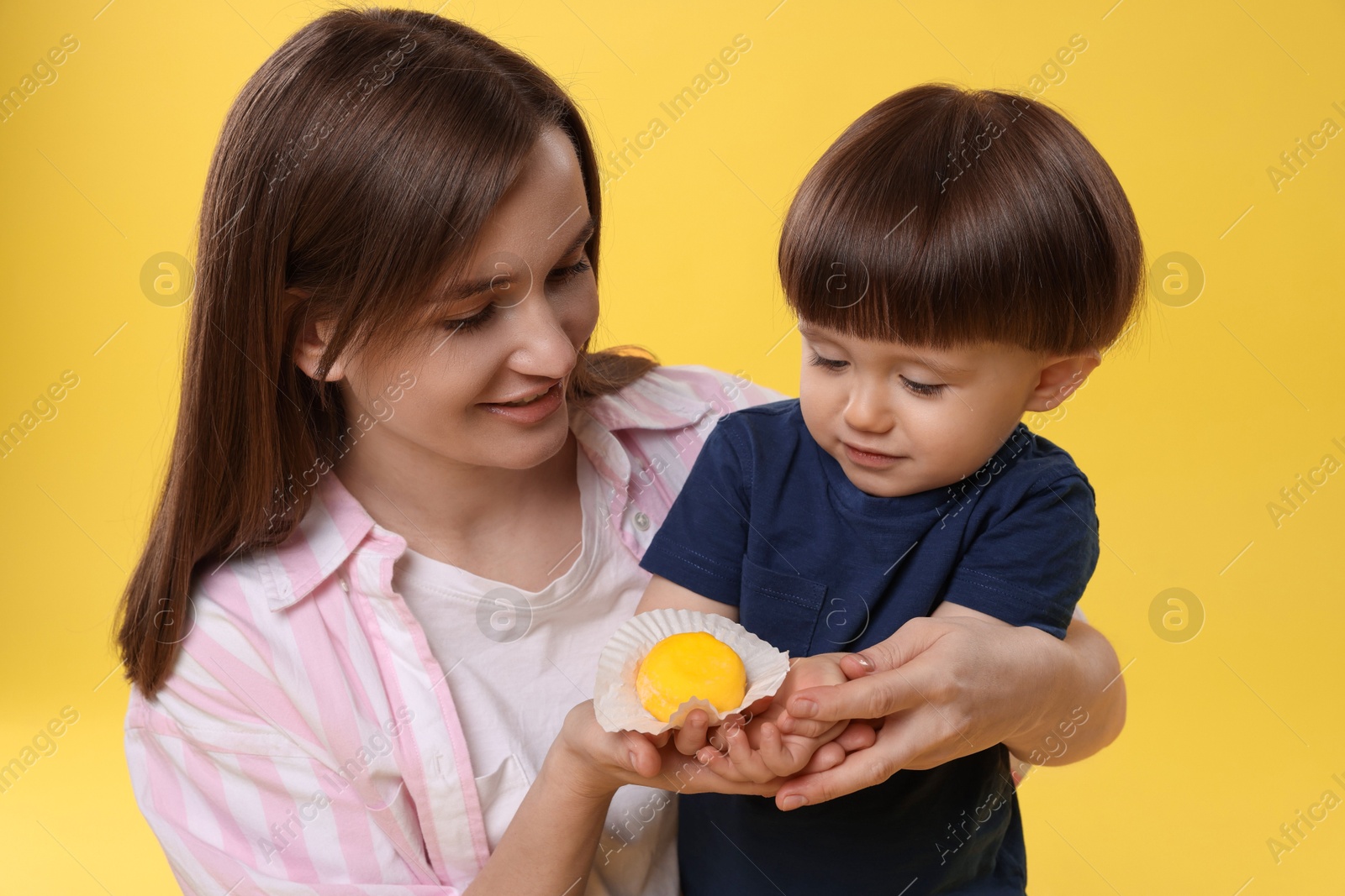 Photo of Mother and baby eating tasty mochi on yellow background