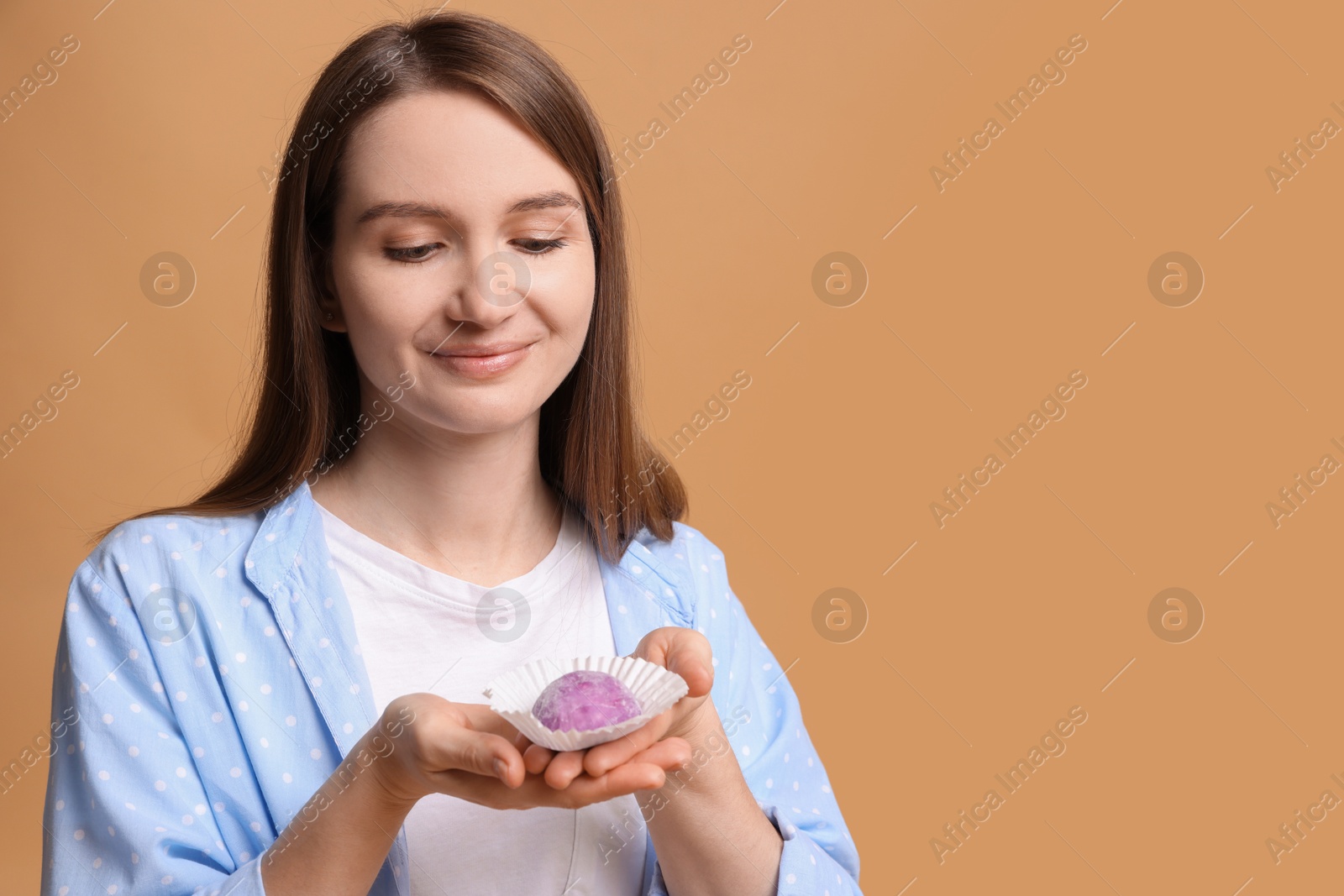 Photo of Woman with tasty mochi on light brown background. Space for text