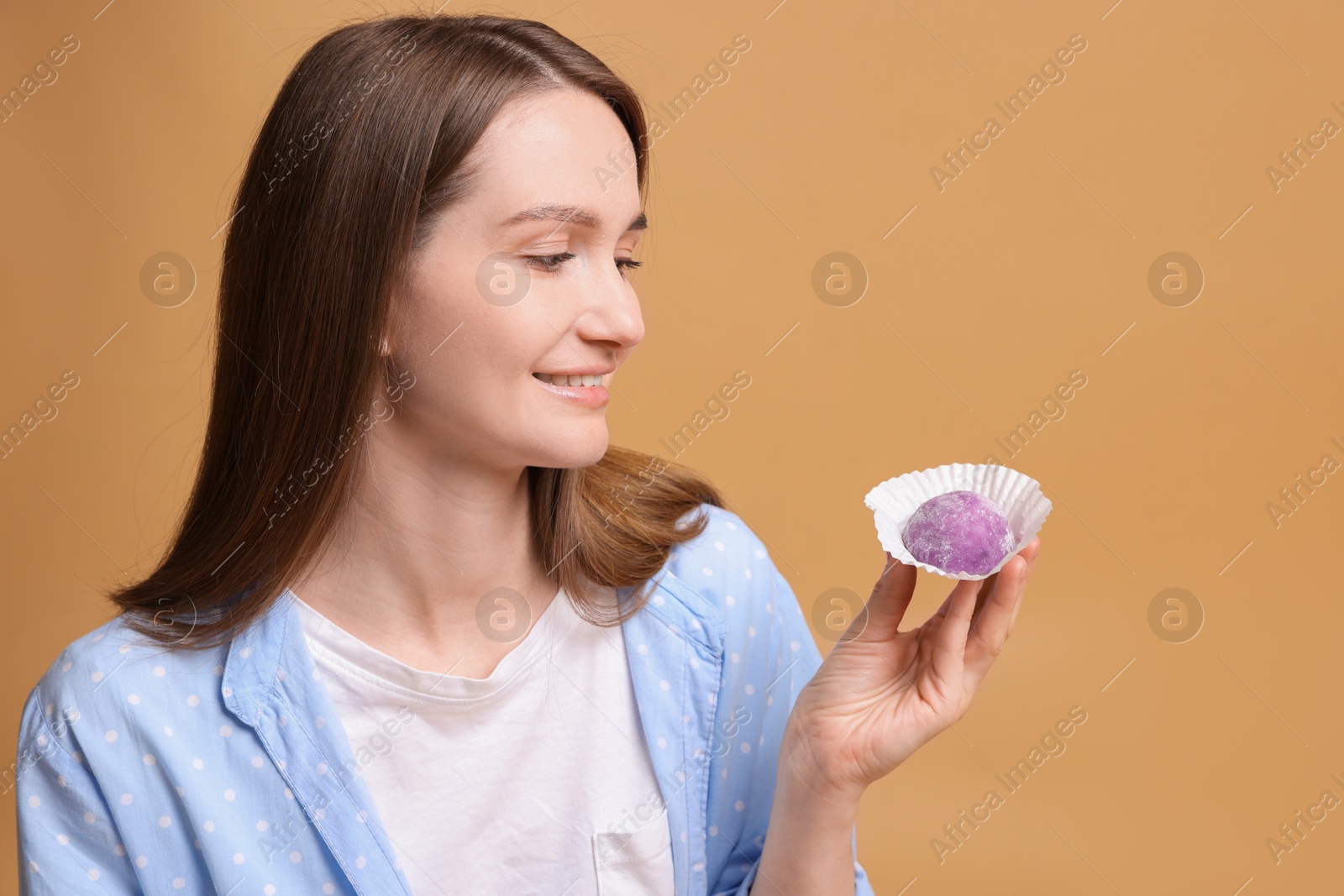 Photo of Woman with tasty mochi on light brown background. Space for text