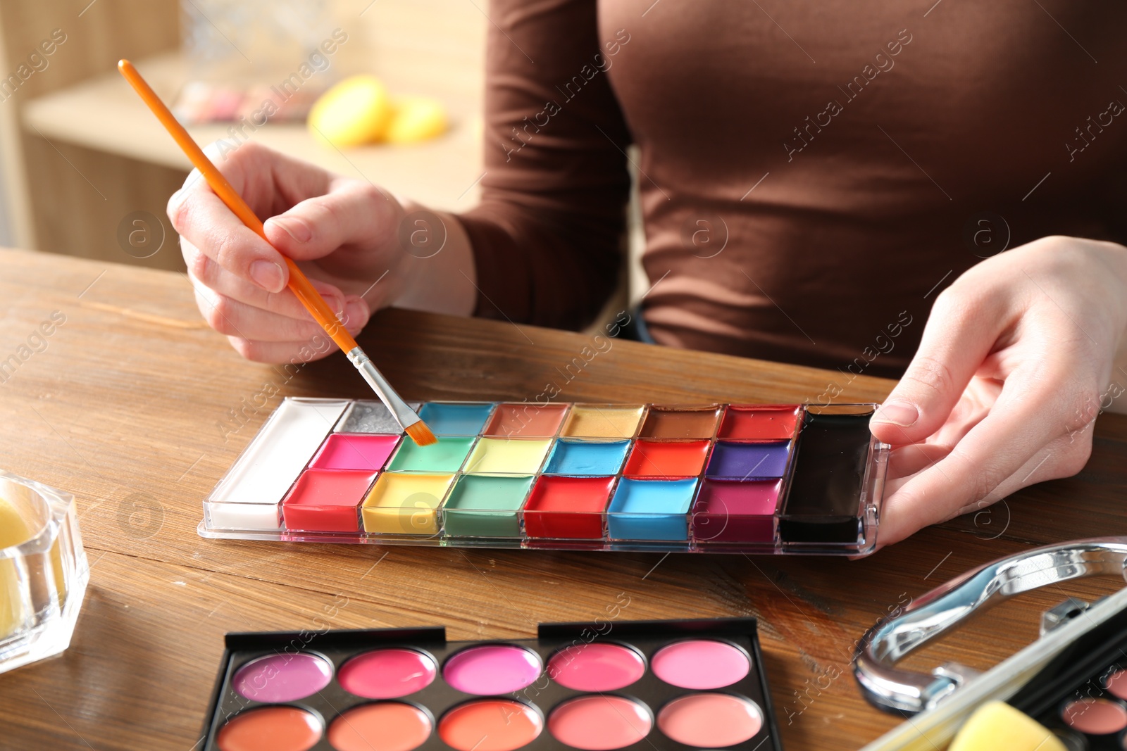 Photo of Professional artist with face painting products and tools at wooden table, closeup