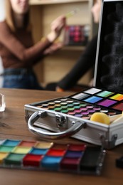 Photo of Face paints on wooden table and artist working with client indoors, selective focus