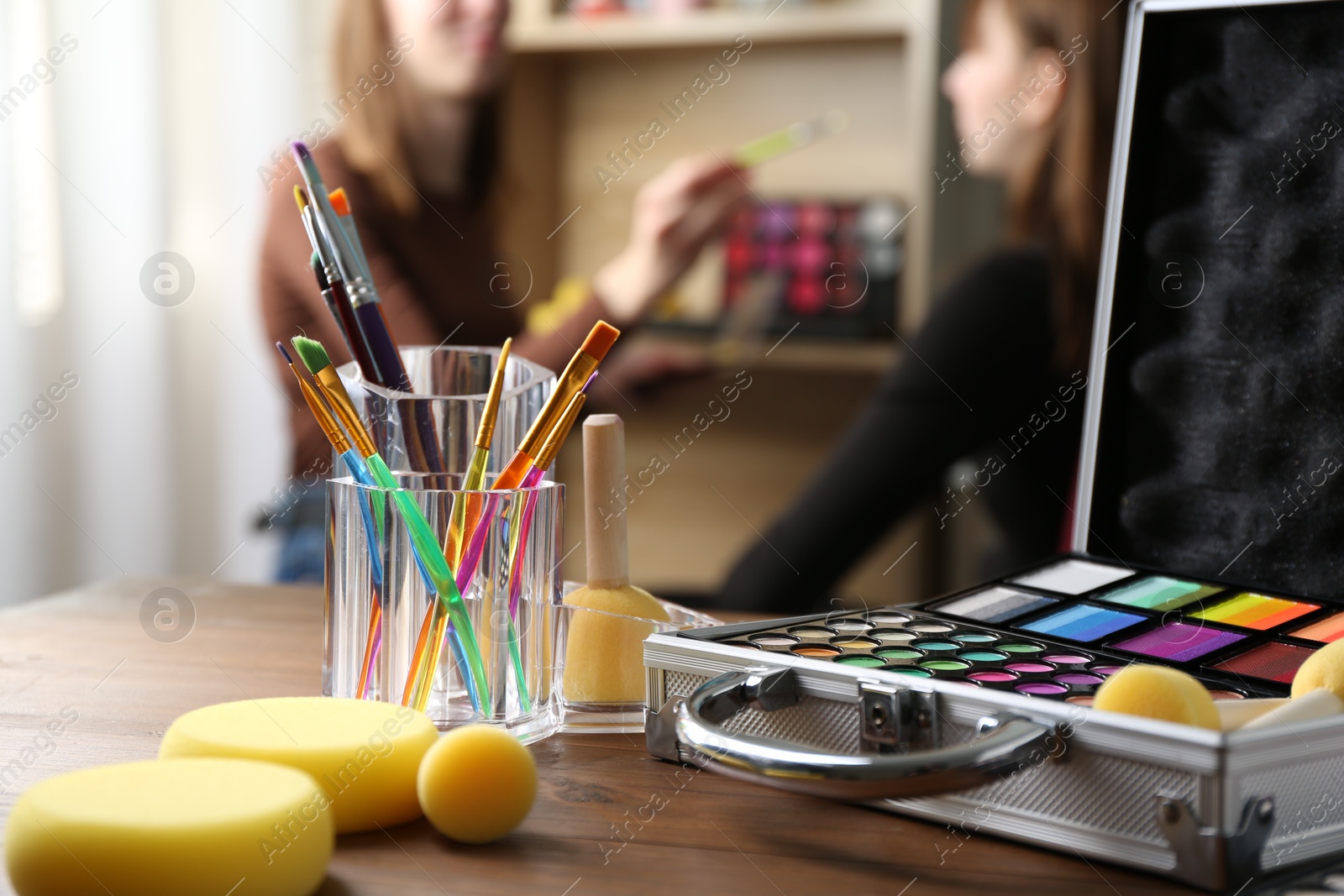 Photo of Face paints on wooden table and artist working with client indoors, selective focus