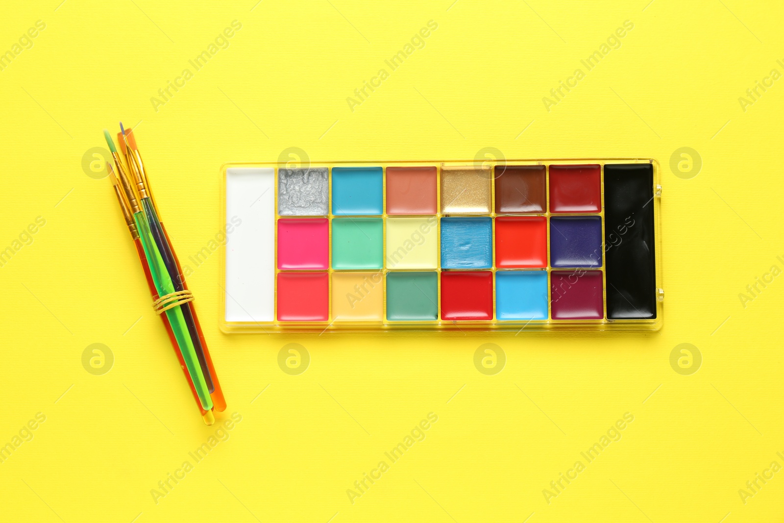 Photo of Face paint palette and brushes on yellow background, top view