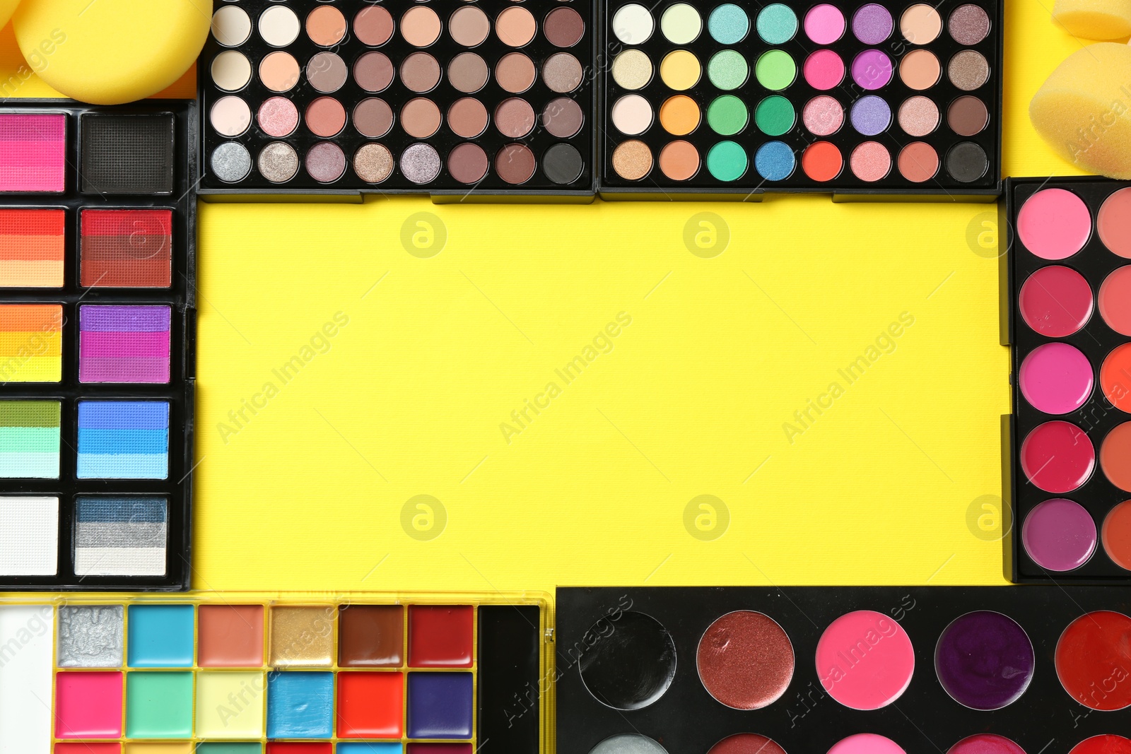 Photo of Frame of face paints and makeup products on yellow background, top view. Space for text