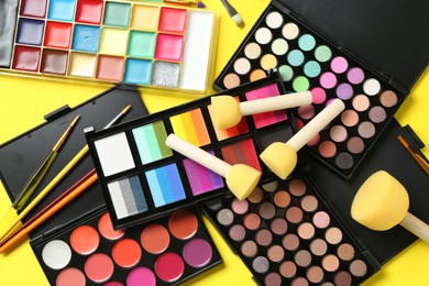 Photo of Face paints, tools and makeup products on yellow background, flat lay