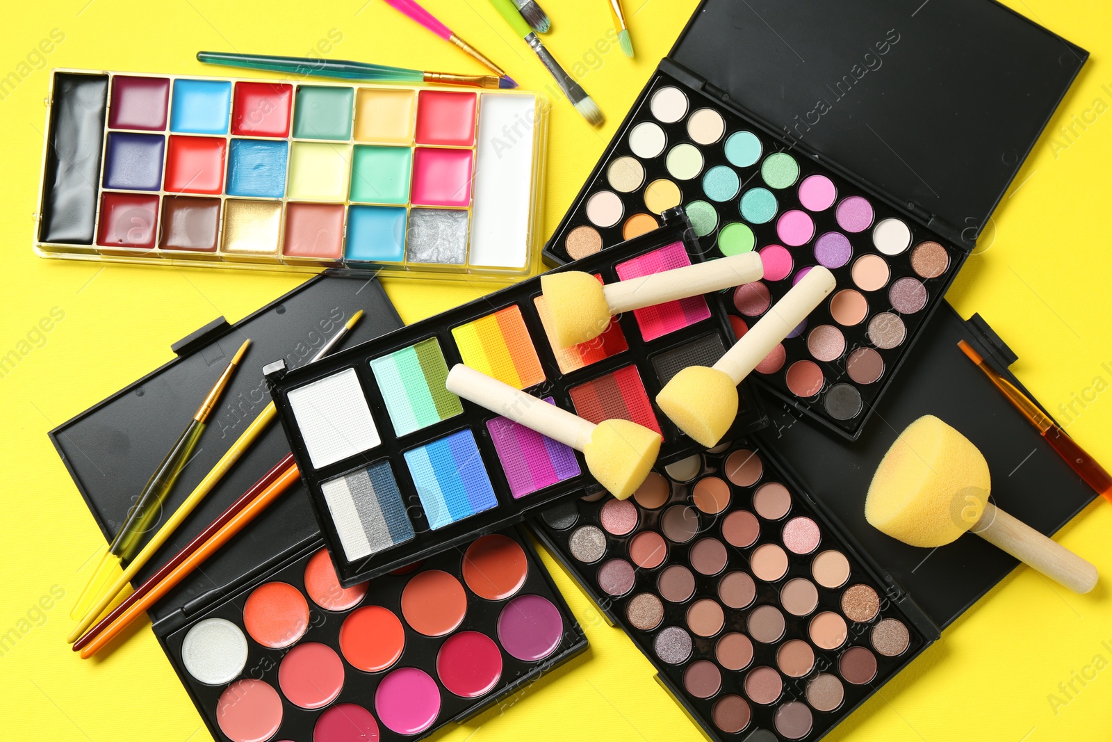 Photo of Face paints, tools and makeup products on yellow background, flat lay