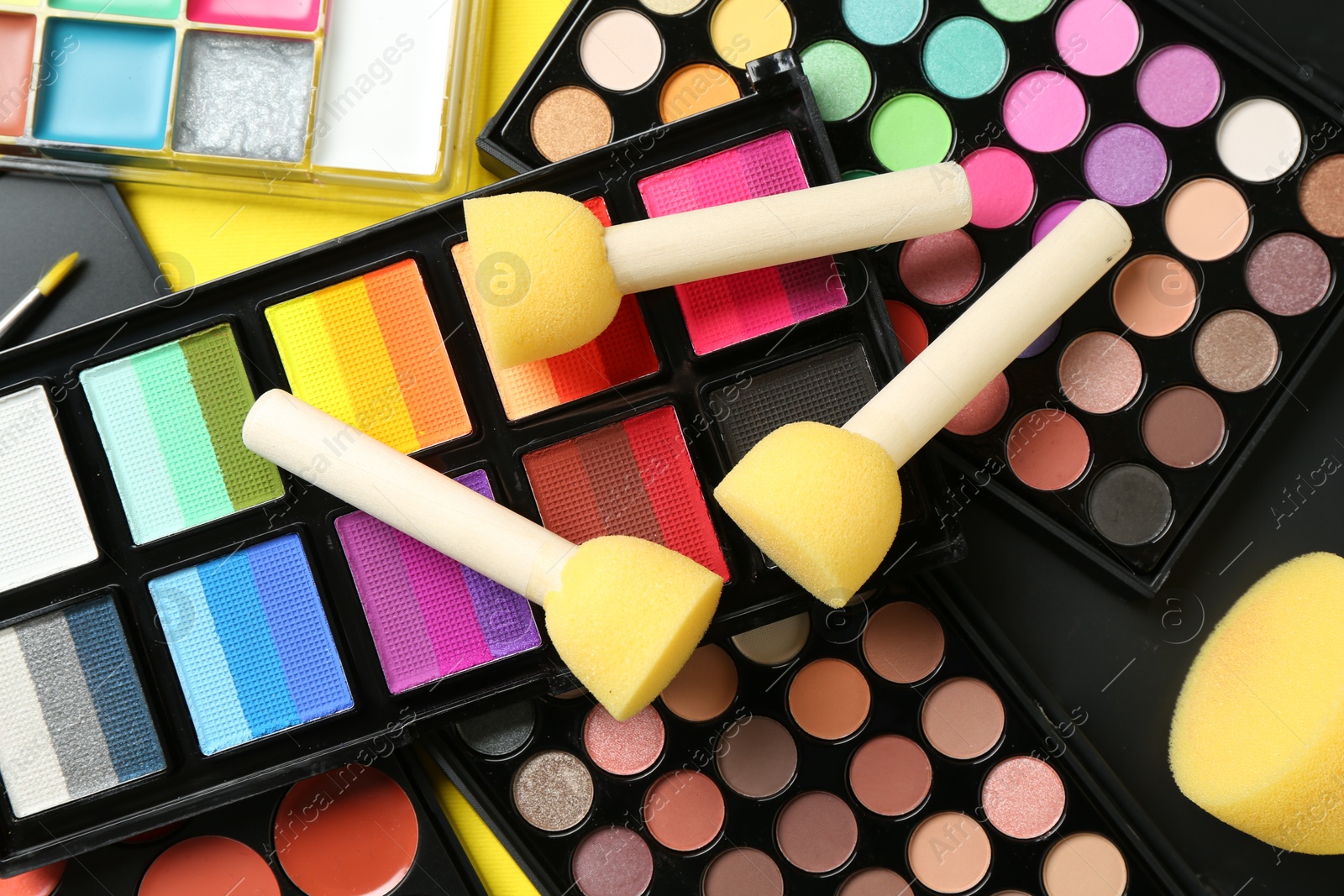 Photo of Face paints, tools and makeup products on yellow background, closeup