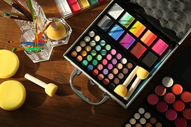 Photo of Face paints and tools on wooden background, flat lay