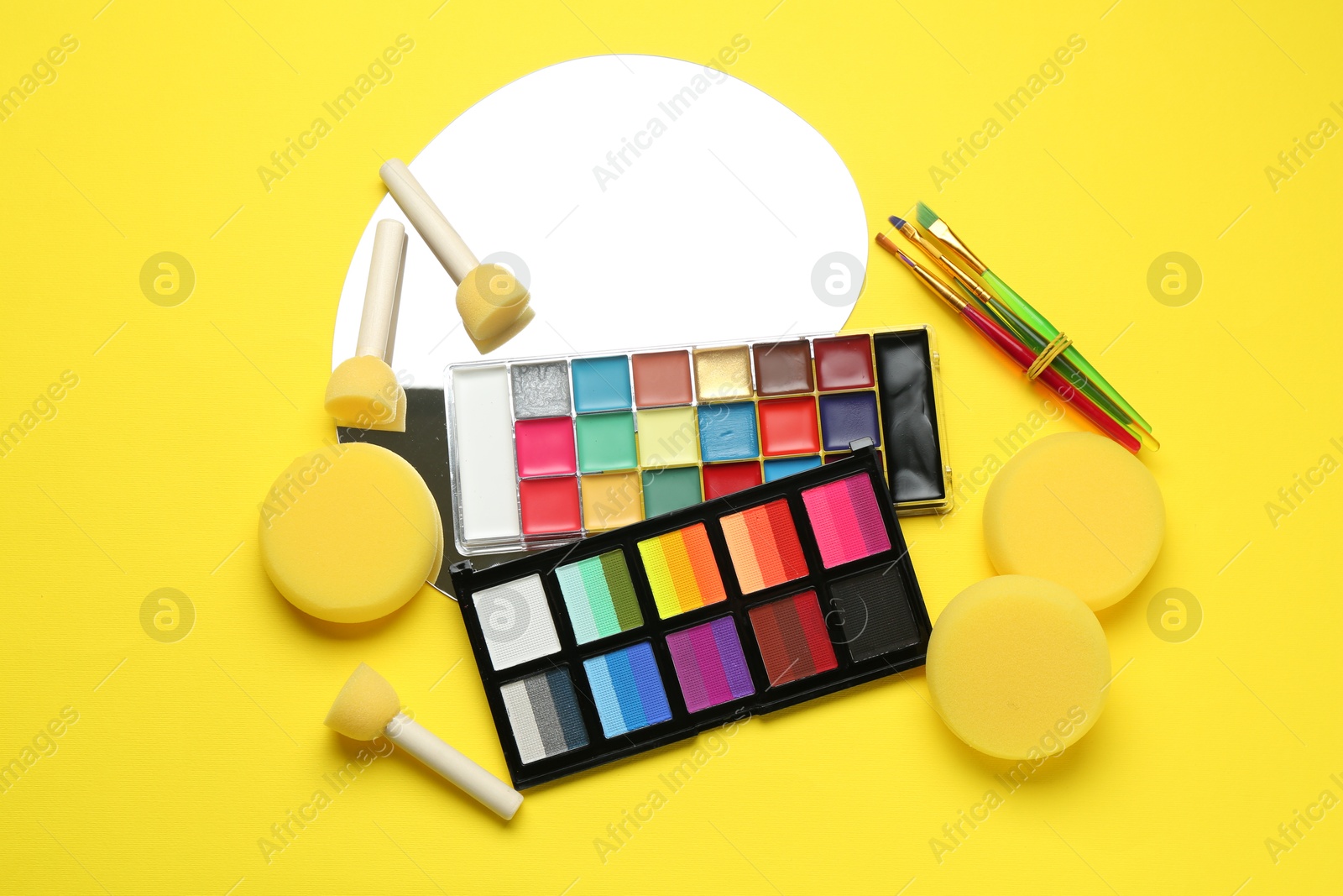 Photo of Face paints and tools on yellow background, flat lay