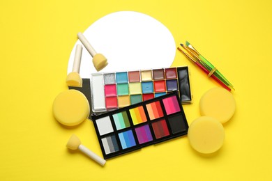 Photo of Face paints and tools on yellow background, flat lay