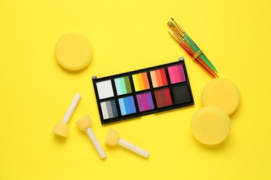 Photo of Face paints and tools on yellow background, flat lay