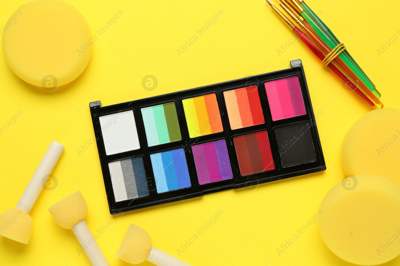 Photo of Face paints and tools on yellow background, flat lay