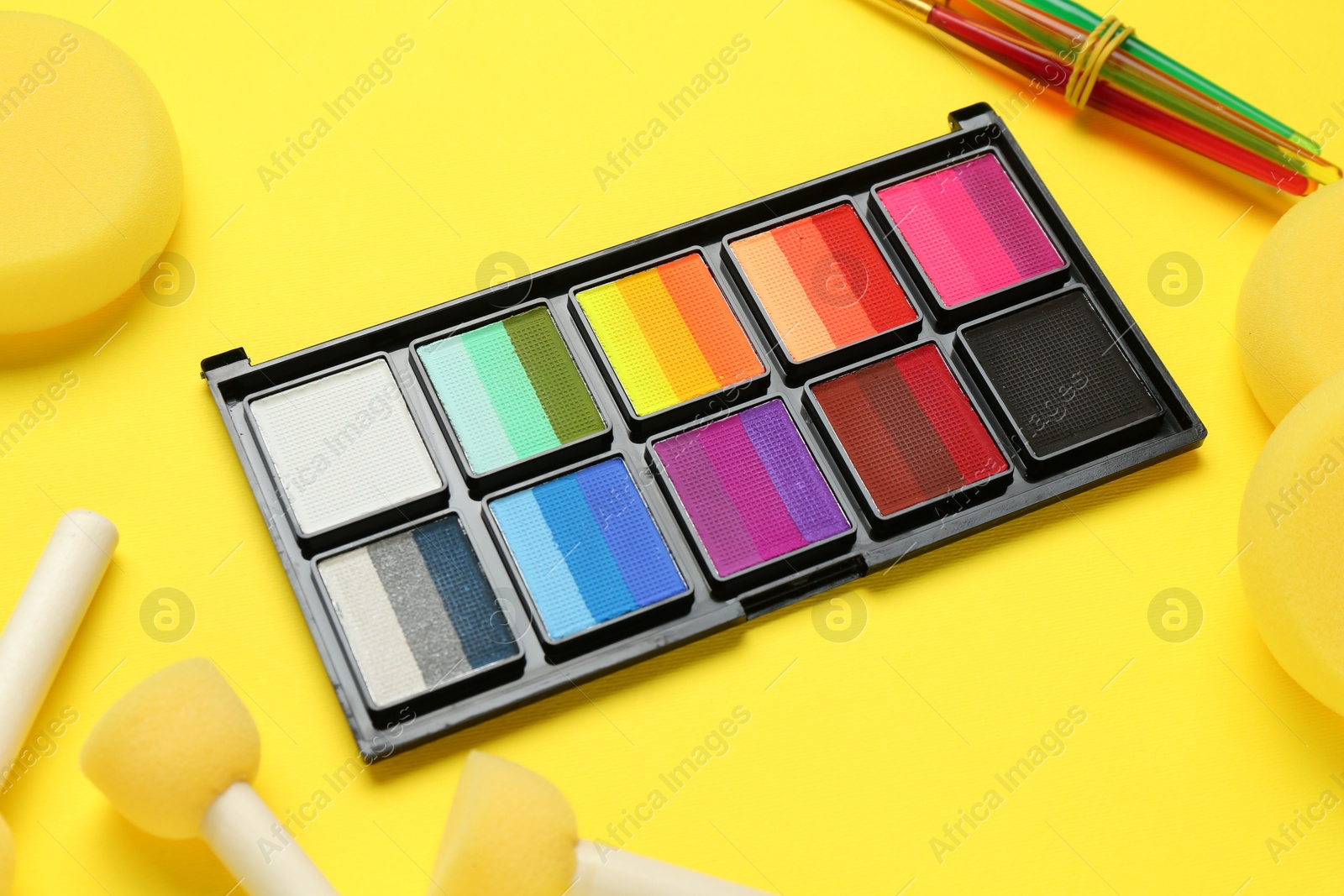 Photo of Face paints and tools on yellow background, closeup