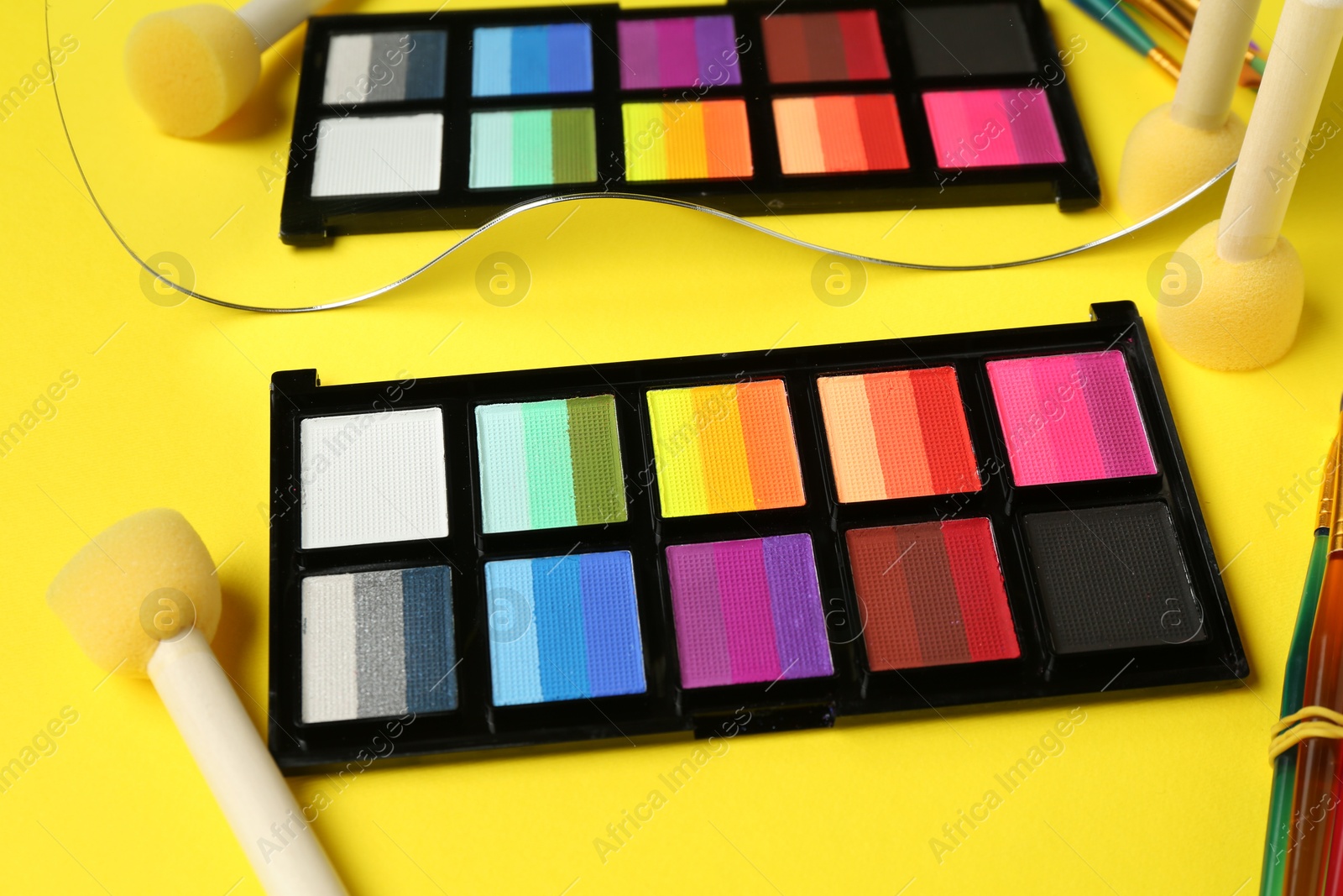 Photo of Face paints and tools on yellow background, closeup