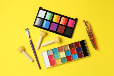 Photo of Face paints and tools on yellow background, flat lay