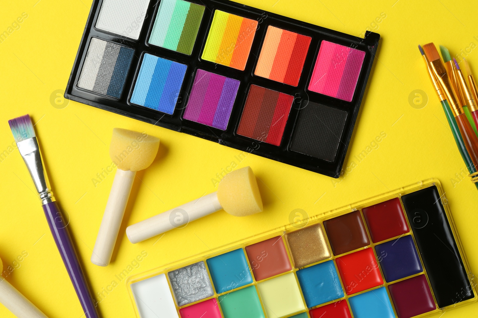 Photo of Face paints and tools on yellow background, flat lay