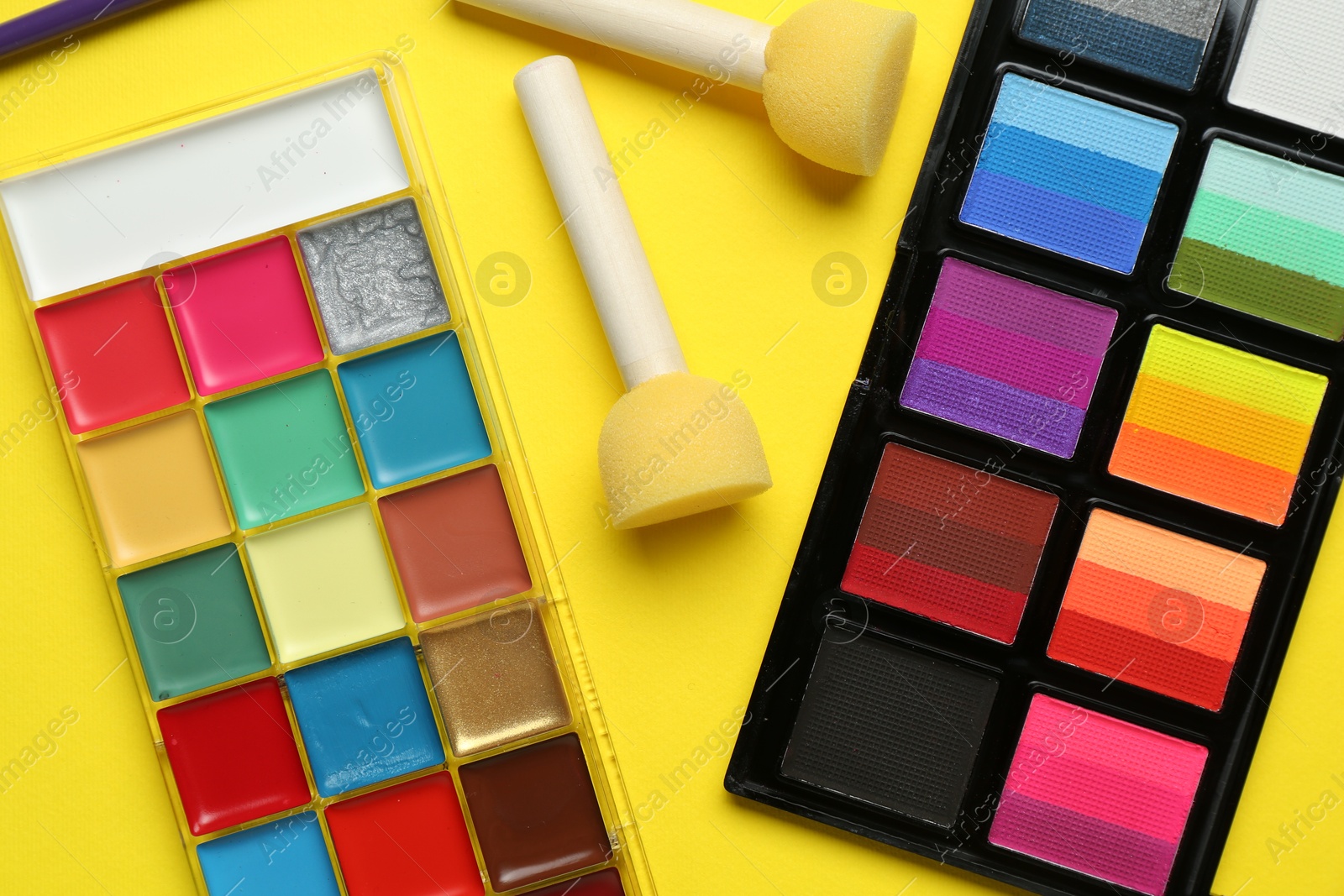 Photo of Face paints and tools on yellow background, flat lay