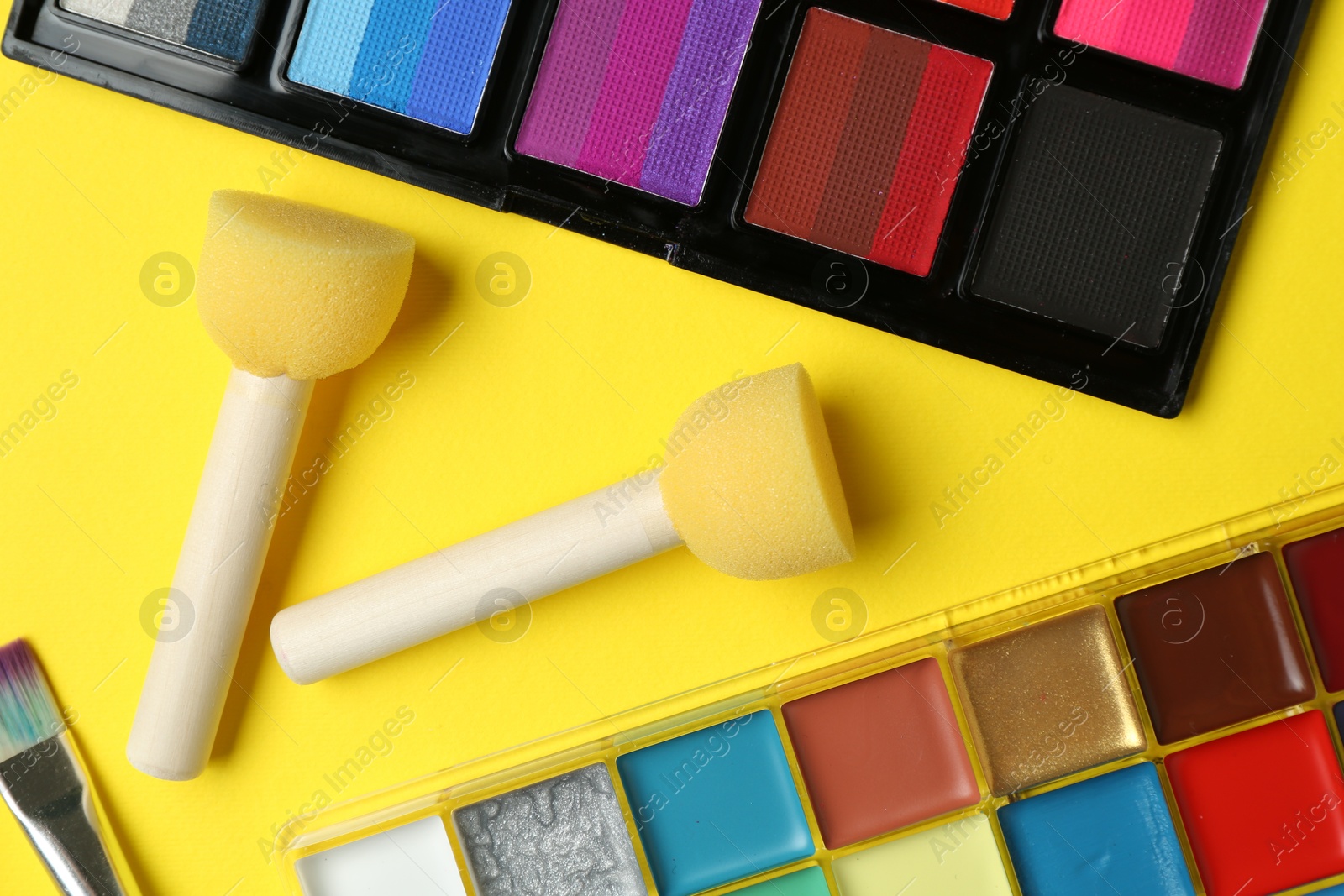 Photo of Face paints and tools on yellow background, flat lay