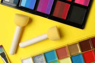 Photo of Face paints and tools on yellow background, flat lay