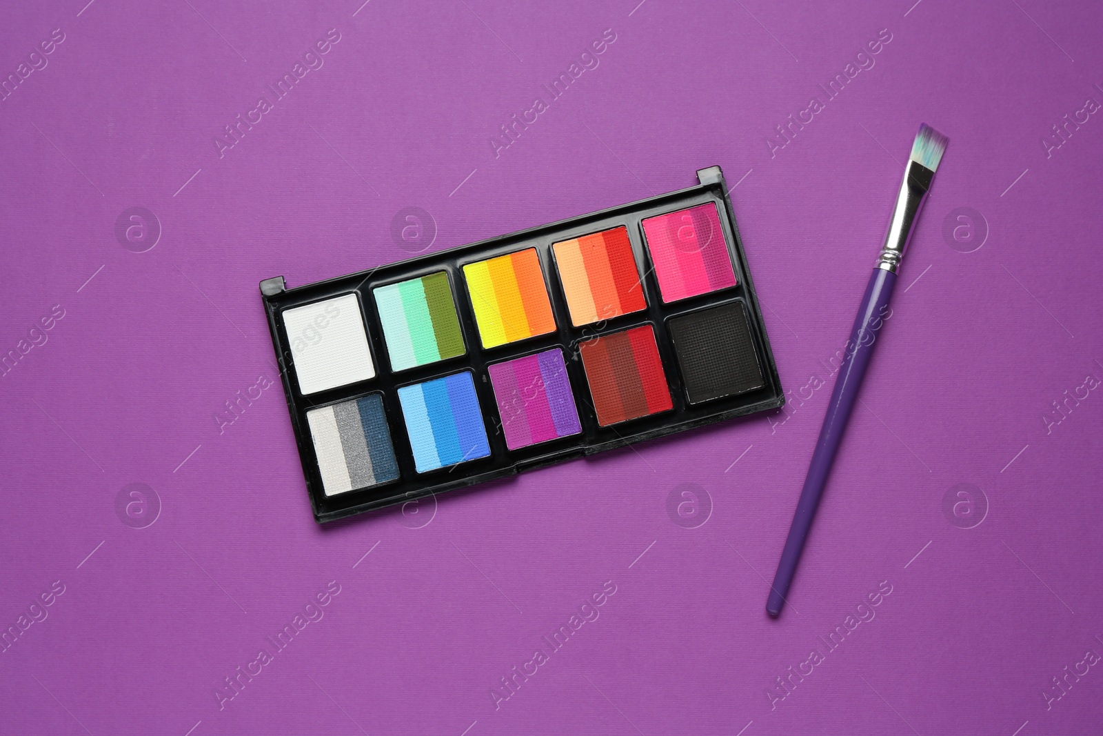 Photo of Face paints and brush on purple background, top view