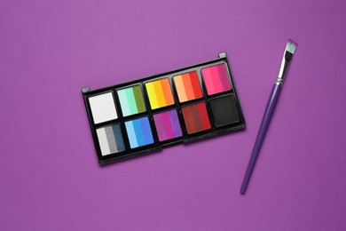 Photo of Face paints and brush on purple background, top view