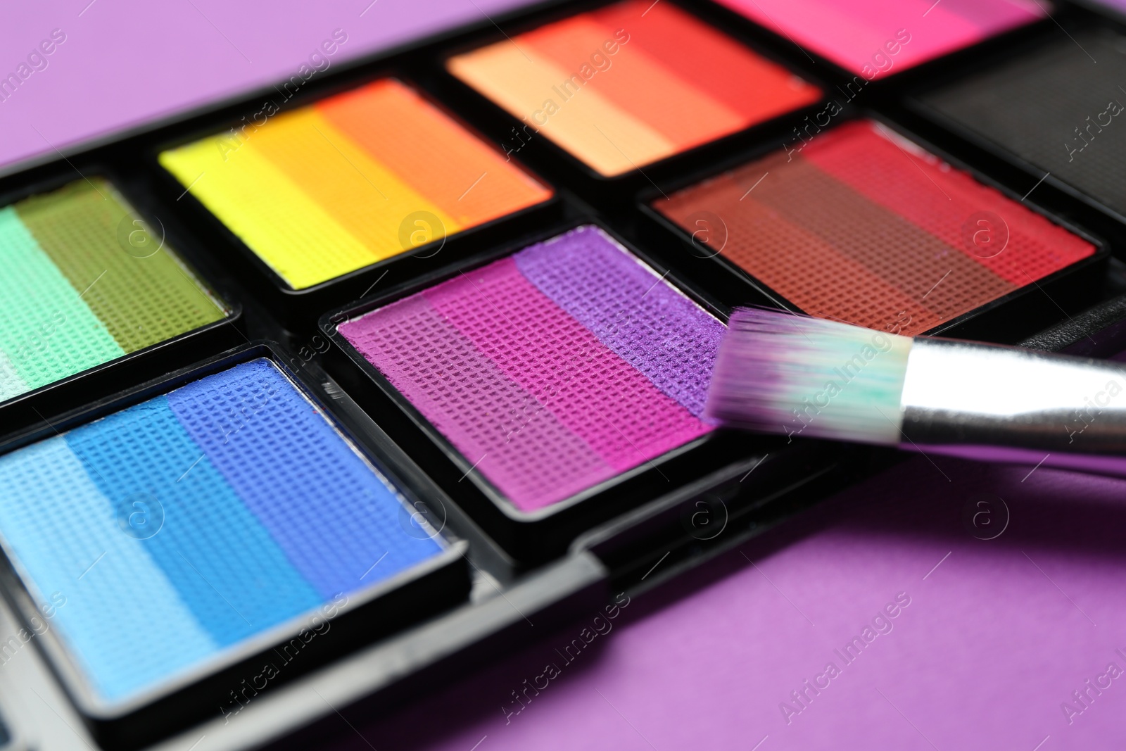 Photo of Face paints and brush on purple background, closeup