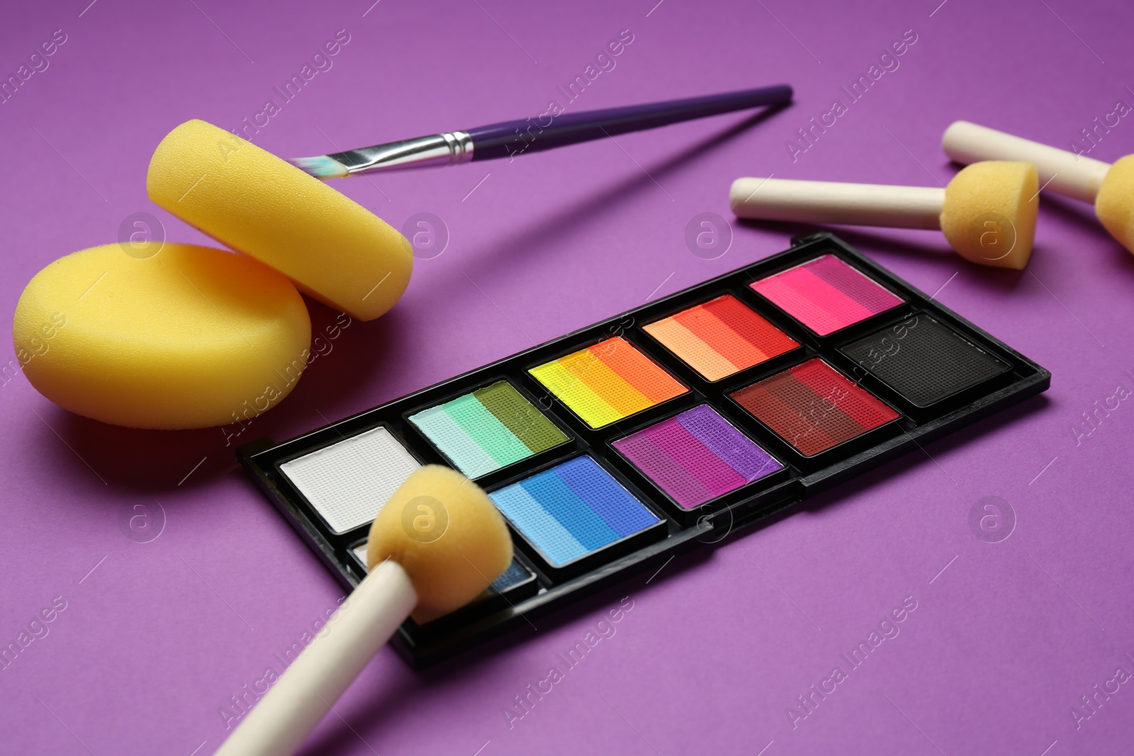 Photo of Face paints and tools on purple background, closeup