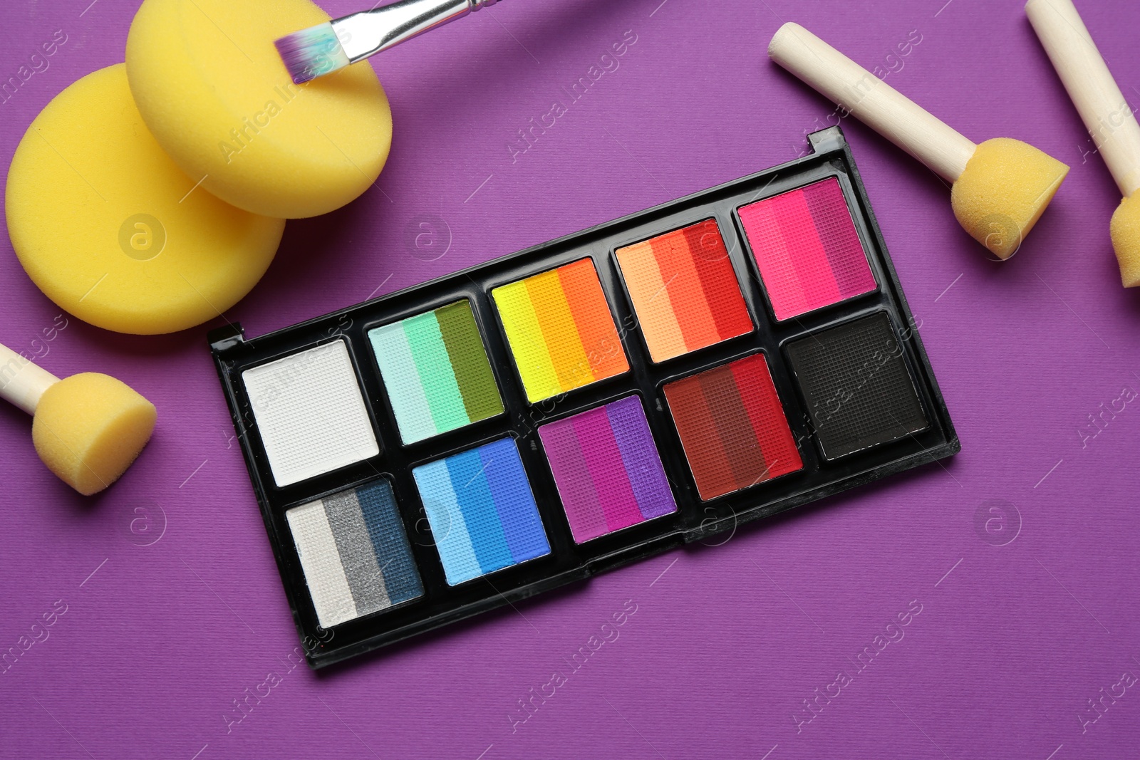 Photo of Face paints and tools on purple background, flat lay