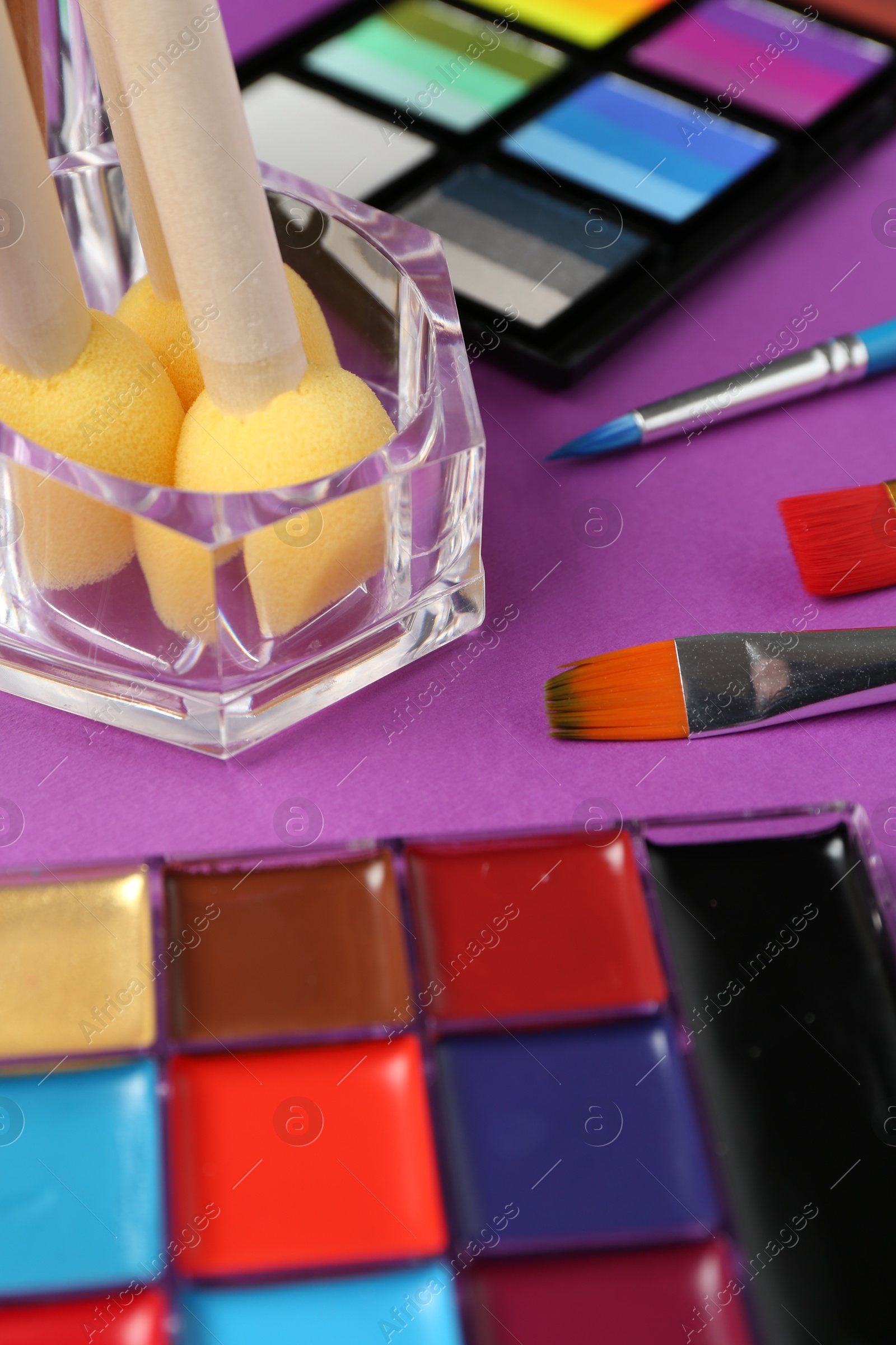 Photo of Face paints and tools on purple background, closeup