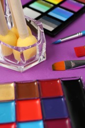 Photo of Face paints and tools on purple background, closeup