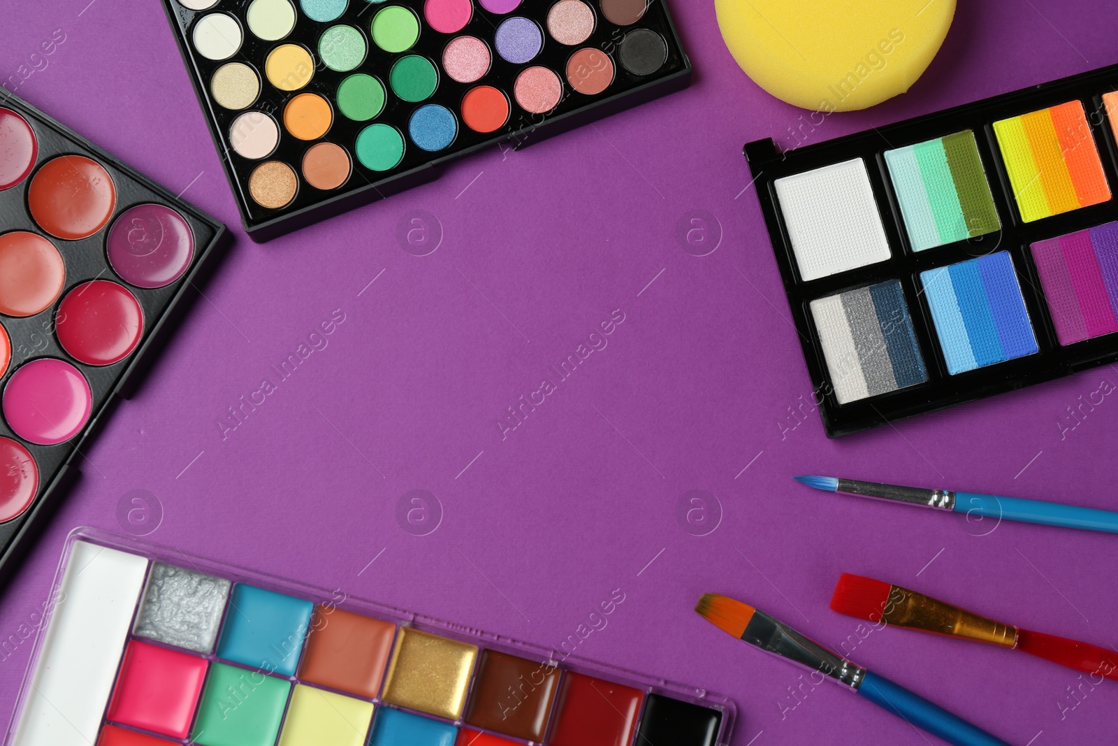 Photo of Frame of face paints and tools on purple background, flat lay. Space for text