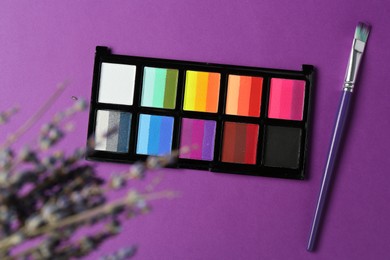 Photo of Face paints and brush on purple background, top view