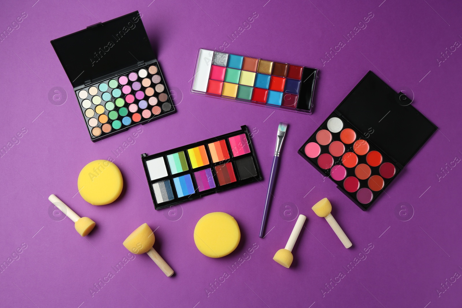 Photo of Face paints, tools and makeup products on purple background, flat lay