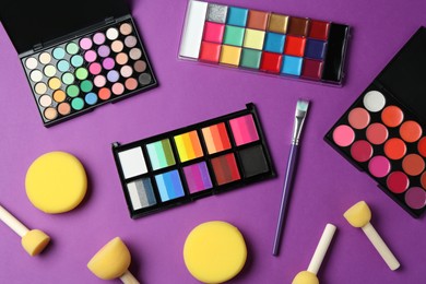 Photo of Face paints, tools and makeup products on purple background, flat lay