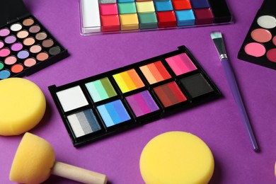 Photo of Face paints, tools and makeup products on purple background, closeup