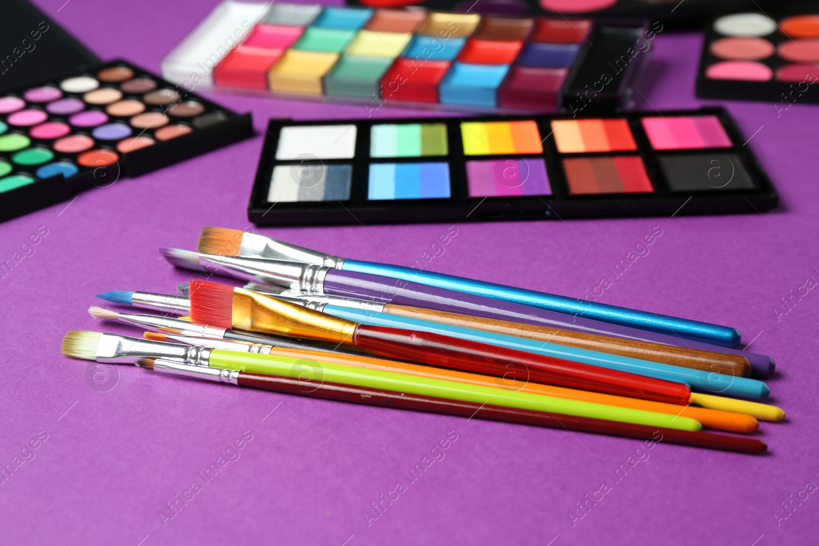 Photo of Face paints, tools and makeup products on purple background, closeup