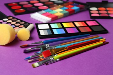 Photo of Face paints, tools and makeup products on purple background, closeup