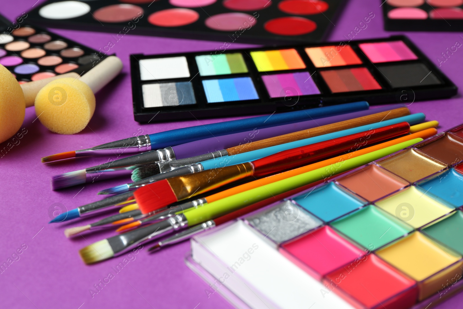 Photo of Face paints, tools and makeup products on purple background, closeup