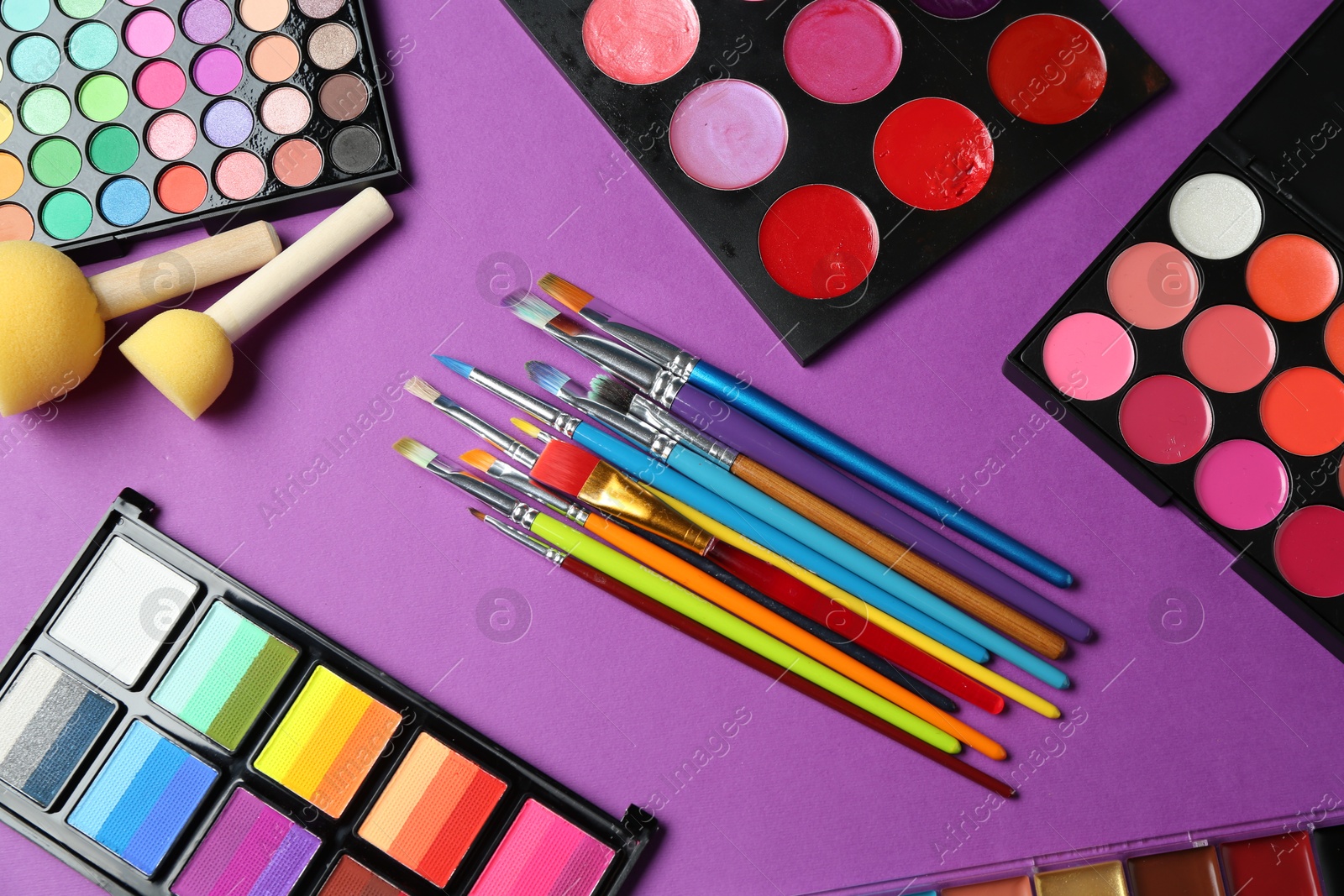 Photo of Face paints, tools and makeup products on purple background, flat lay