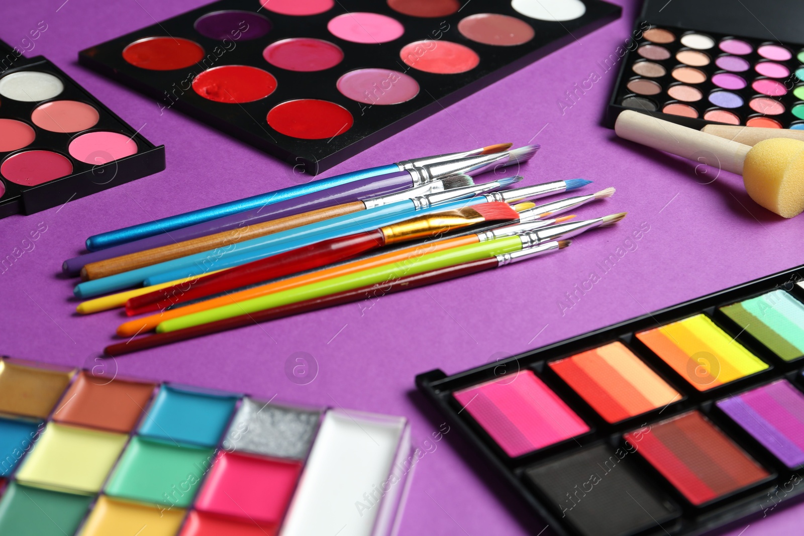 Photo of Face paints, tools and makeup products on purple background, closeup