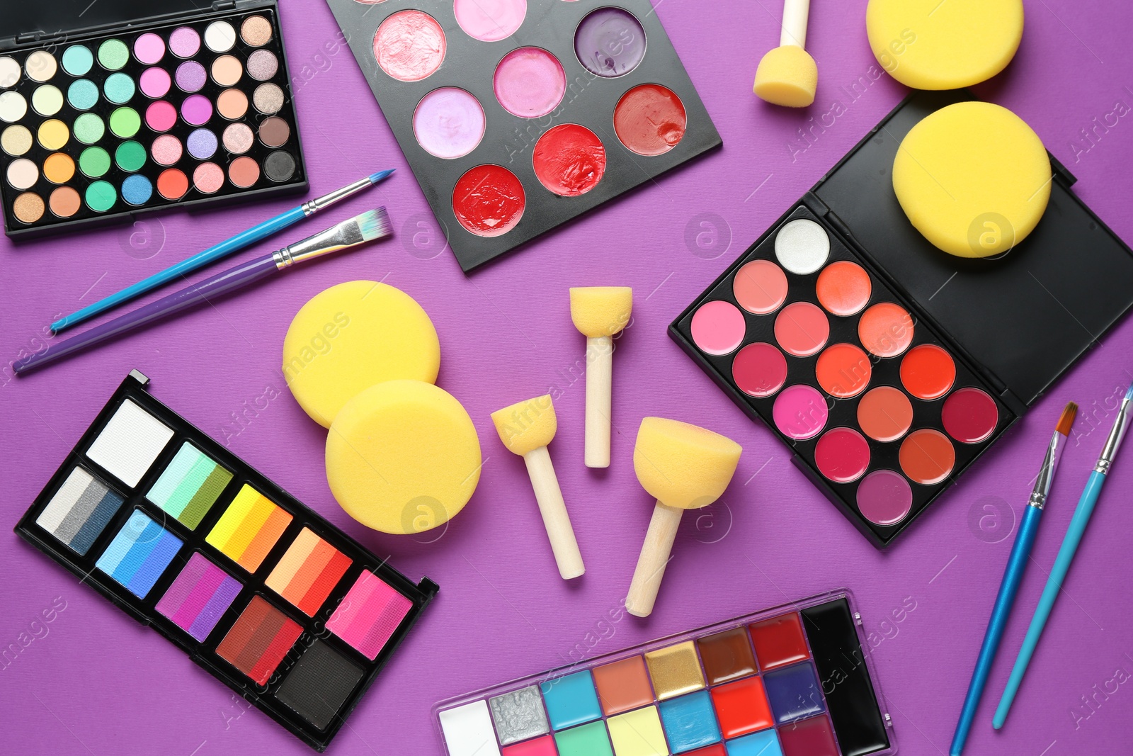 Photo of Face paints, tools and makeup products on purple background, flat lay