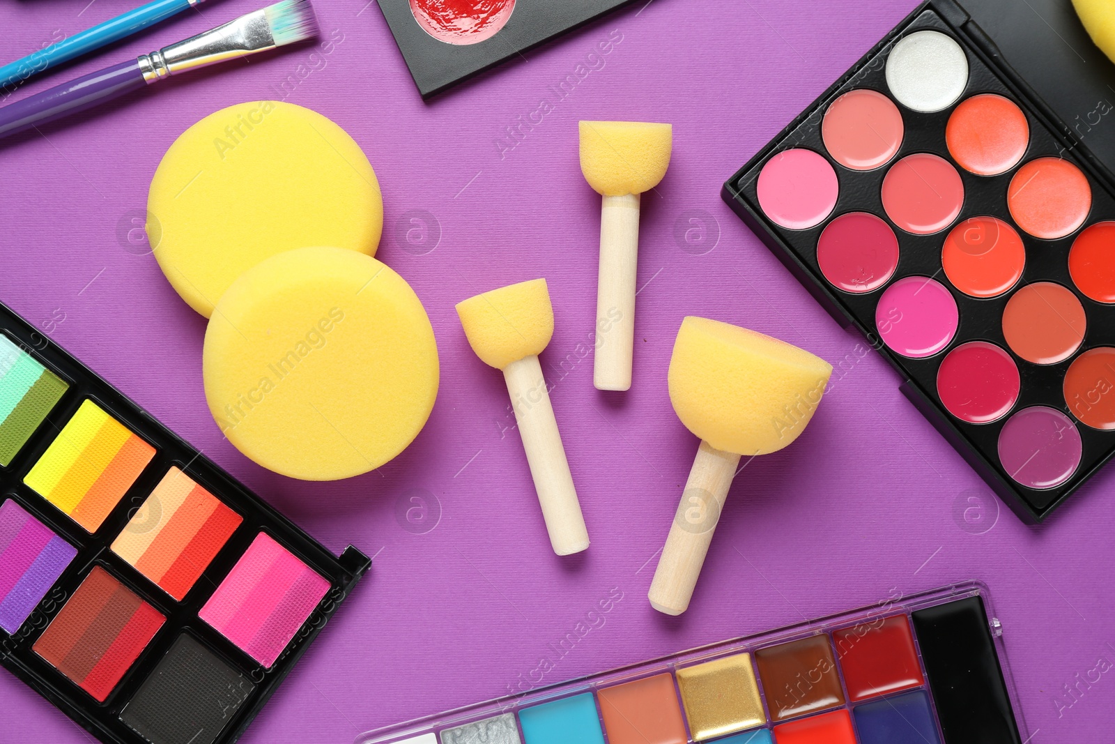 Photo of Face paints and tools on purple background, flat lay