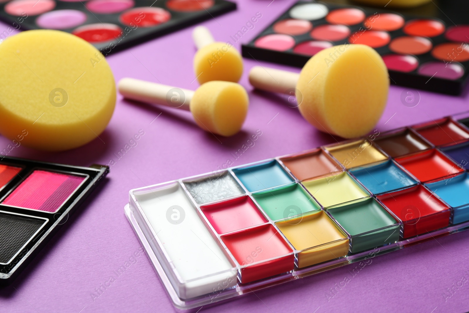 Photo of Face paints and tools on purple background, closeup